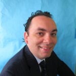 A man in a suit and tie smiling for the camera. A man in a suit and tie smiling for the camera.