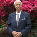 A man in a suit standing next to pink flowers.