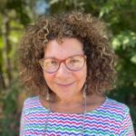 A woman with curly hair wearing glasses and smiling.